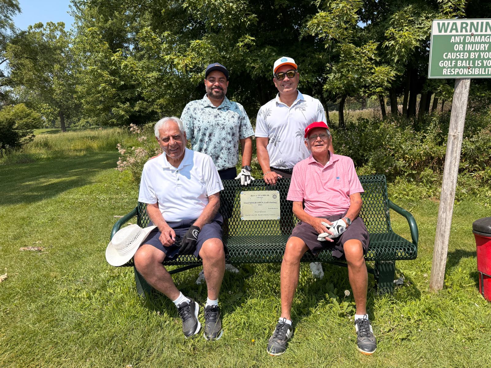 Four golfers around a course bench bearing a 53rd Singh Open Golf Outing plaque