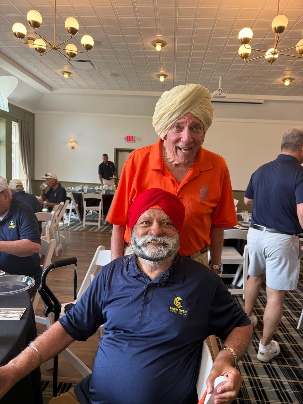 Two Singh Open golfers, one wearing the ceremonial turban and an orange polo, in the clubhouse
